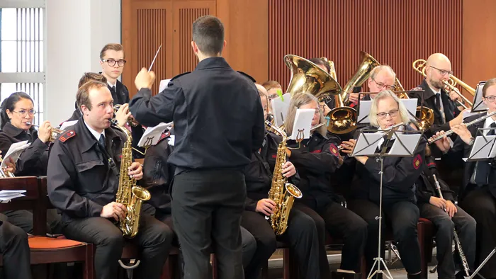 Blasorchester spielt während der Fronleichnamsprozession in St. Laurentius Plettenberg-Herscheid. Die Musiker tragen dunkle Uniformen und spielen verschiedene Instrumente wie Saxophone, Posaunen und Tuba.