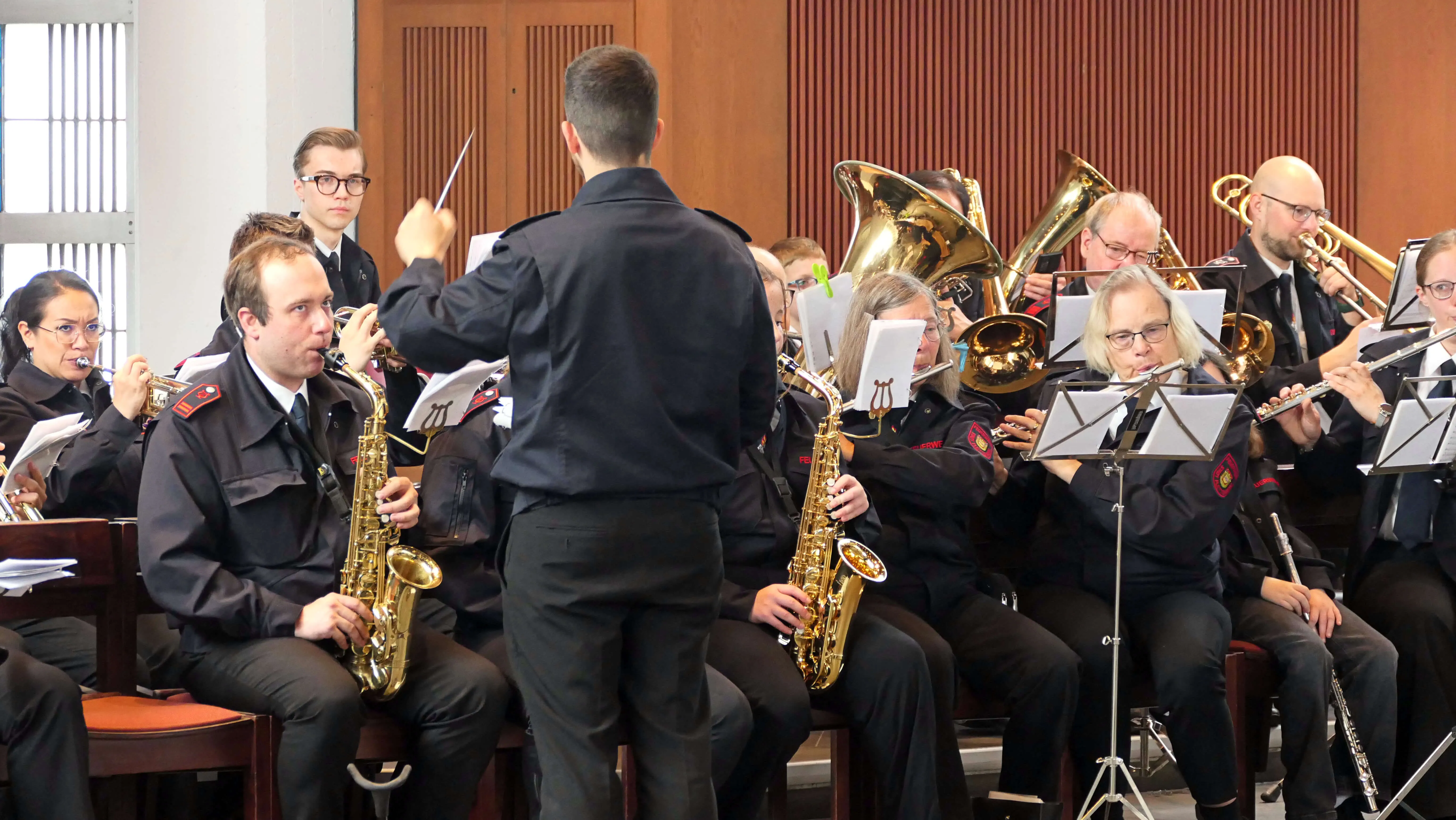 Blasorchester spielt während der Fronleichnamsprozession in St. Laurentius Plettenberg-Herscheid. Die Musiker tragen dunkle Uniformen und spielen verschiedene Instrumente wie Saxophone, Posaunen und Tuba.