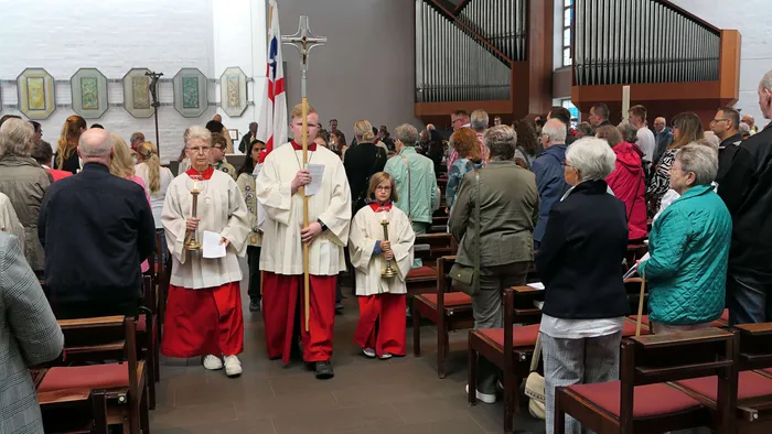 Eine Prozession mit Geistlichen und Ministranten schreitet durch die Kirche, während Gemeindemitglieder auf Bänken sitzen und zusehen.
