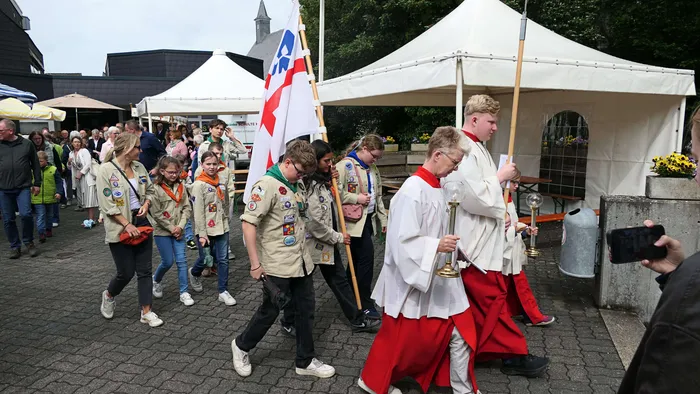 Eine Prozession mit Pfadfindern und einem Geistlichen mit einer Monstranz zieht vor Zuschauern an einem Gebäude vorbei.