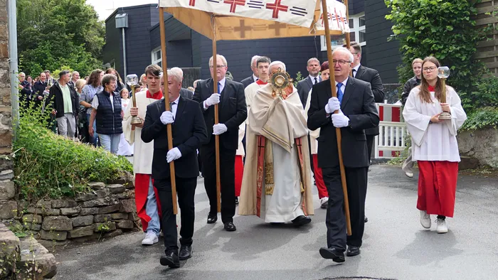Eine Prozession mit Geistlichen und Ministranten zieht auf einer Straße vor Zuschauern vorbei. Ein Geistlicher trägt eine Monstranz.
