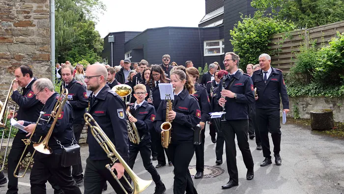 Eine Blaskapelle in Uniformen marschiert während einer Prozession durch eine Straße, umgeben von Zuschauern.