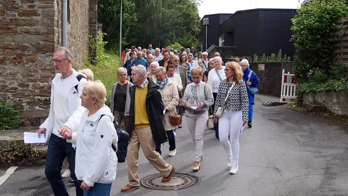 Eine große Gruppe von Menschen verschiedener Altersgruppen geht auf einer Straße in einer Stadt. Viele tragen festliche Kleidung und einige halten religiöse Gegenstände.