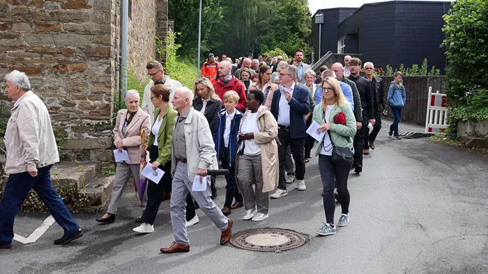 Eine große Gruppe von Menschen verschiedener Altersgruppen geht auf einer Straße in Plettenberg-Herscheid, viele halten Blätter oder andere kleine Gegenstände in den Händen.