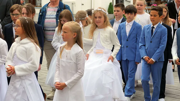 Kinder in festlicher Kleidung stehen während der Fronleichnamsprozession in Plettenberg-Herscheid. Einige tragen weiße Kleider und Kränze, andere blaue Anzüge.