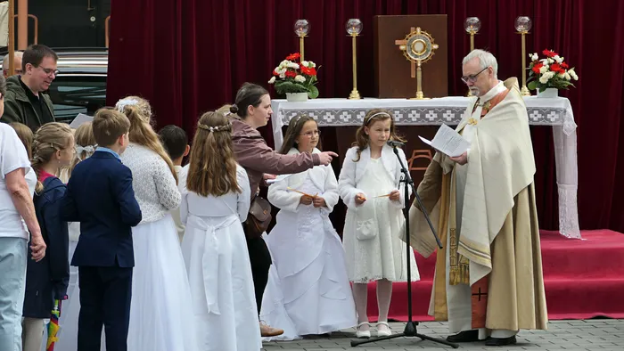 Ein Priester hält während eines Fronleichnamsgottesdienstes in St. Laurentius Plettenberg-Herscheid eine Ansprache vor einer Gruppe von Kommunionskindern in weißen Gewändern.