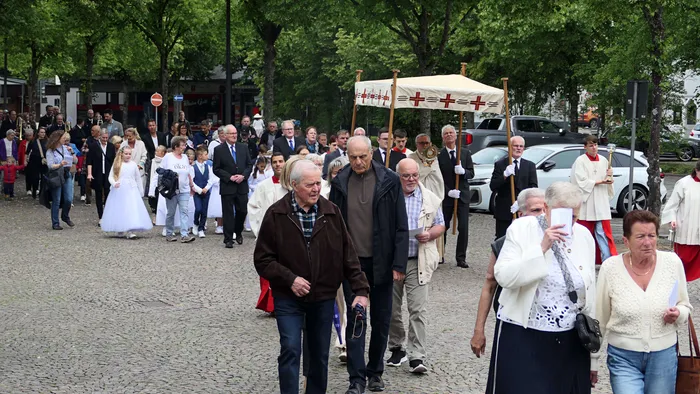 Eine Prozession mit Fahnen und Kommunionskindern zieht durch eine Stadtstraße, umgeben von Zuschauern.