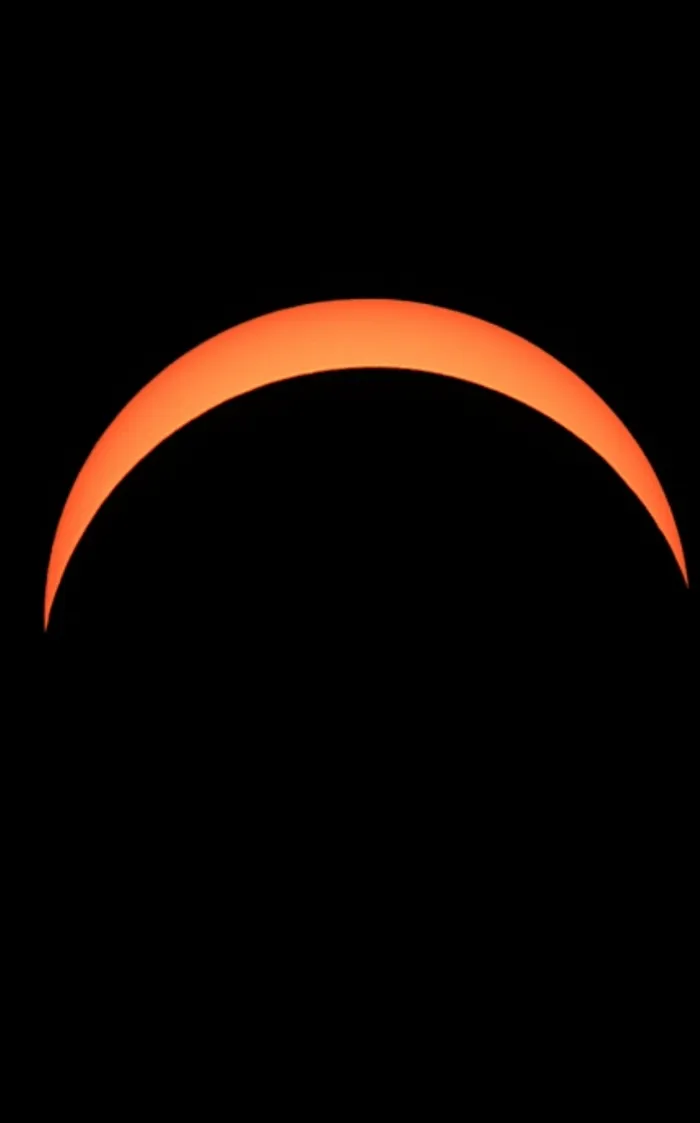 Eine leuchtend orangefarbene Sichel der Sonne vor schwarzem Hintergrund.