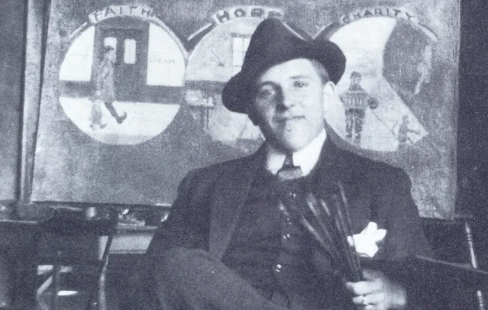 Ernst Geitlinger in Anzug und Hut vor einem Gemälde mit den Motiven „Faith“, „Hope“ und „Charity“.