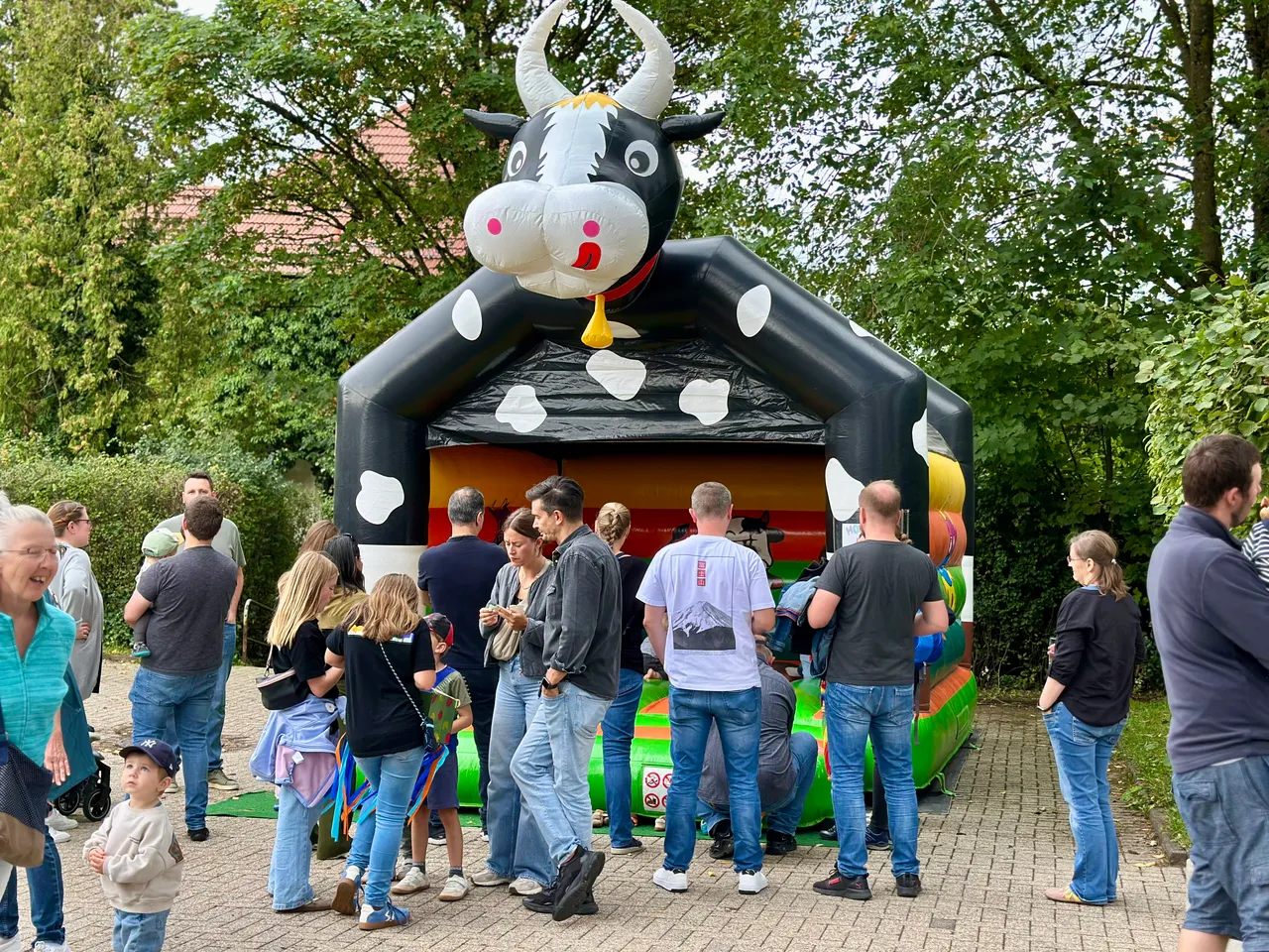 Eine aufblasbare Hüpfburg in Form einer schwarz-weißen Kuh, vor der Menschen bei einem Gemeindefest stehen.