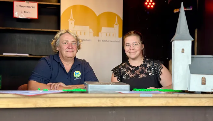 Ein Mann und eine Frau sitzen lächelnd hinter einem Tresen bei einem Gemeindefest der evangelischen Kirchengemeinde Hülscheid-Heedfeld.