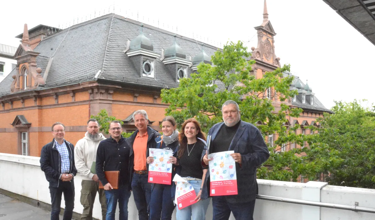 Eine Gruppe von sieben Personen steht vor einem roten Backsteingebäude mit grauem Dach. Sie halten Plakate mit dem Aufdruck „Mensch Altstadt!“ und dem Logo der IHK. Im Hintergrund ist die sanierte Alte Post zu sehen.