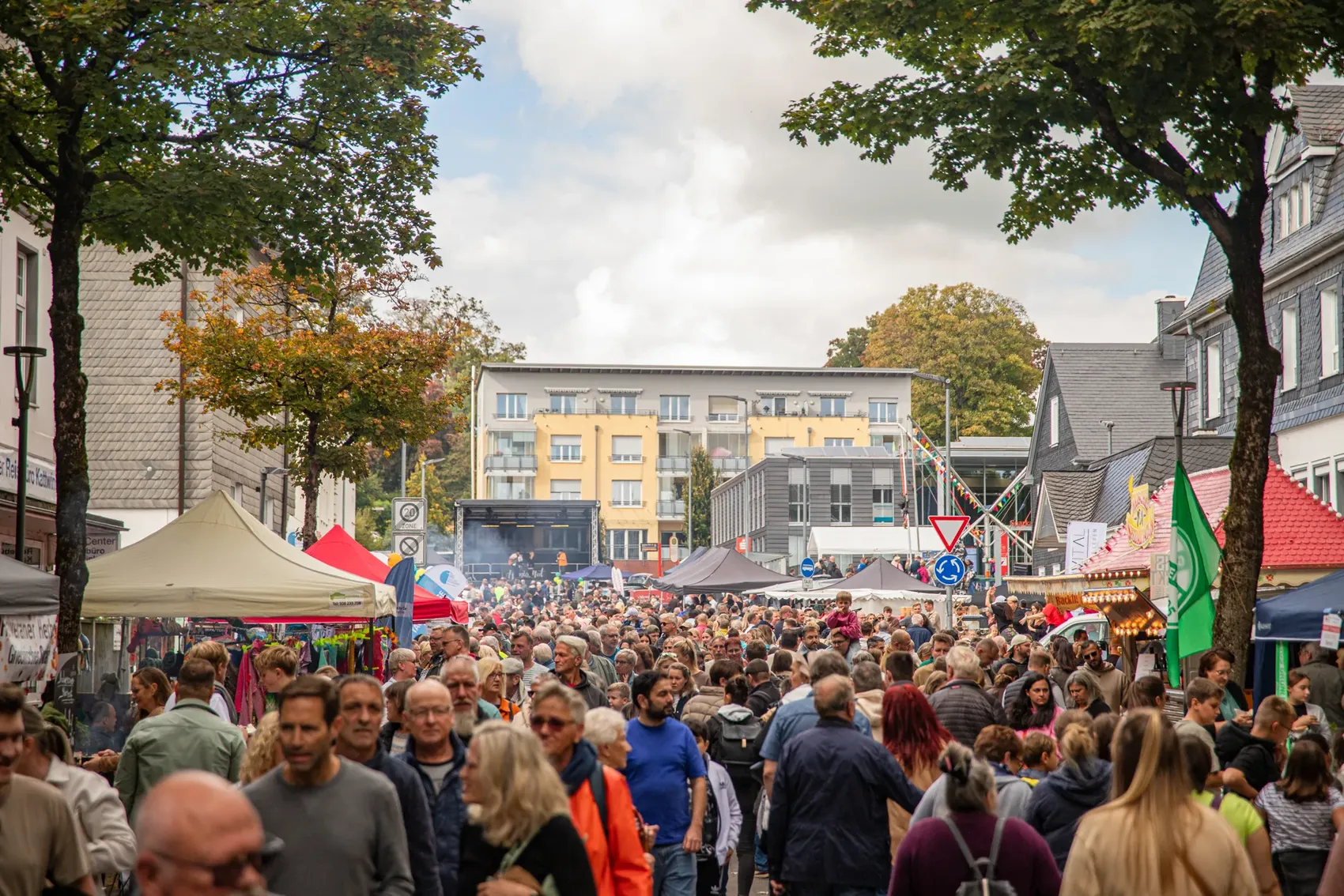Menschenmenge auf einem Stadtfest mit Marktständen und Imbissbuden zwischen Häusern.