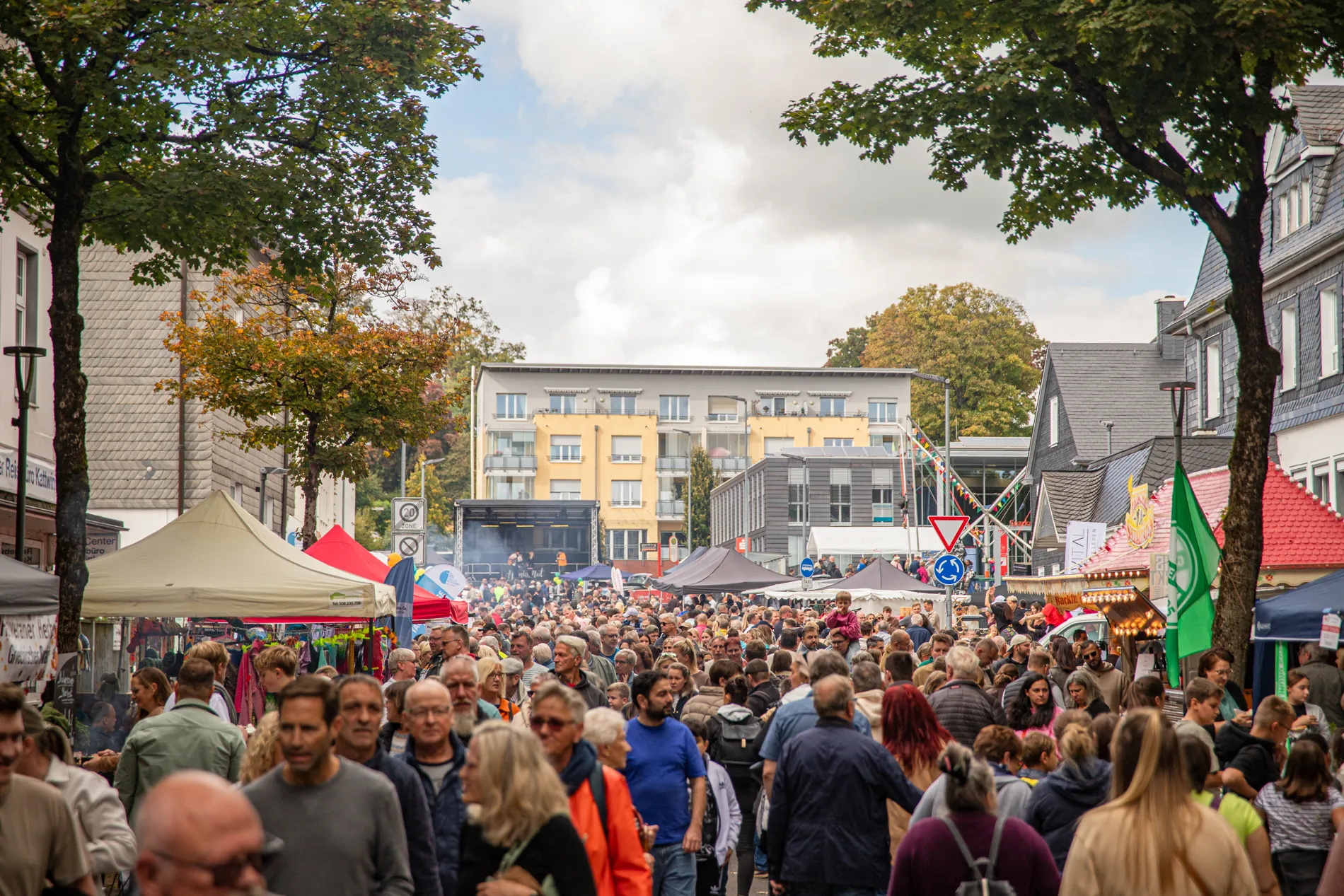 Menschenmenge auf einem Stadtfest mit Marktständen und Imbissbuden zwischen Häusern.