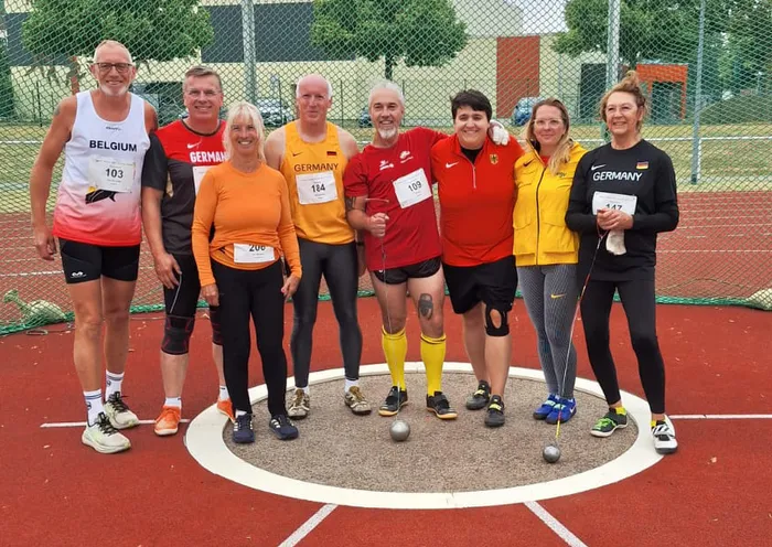Acht Mitglieder der Hammerwurfgruppe posieren gemeinsam in einem Wurfkreis auf einer Sportanlage.