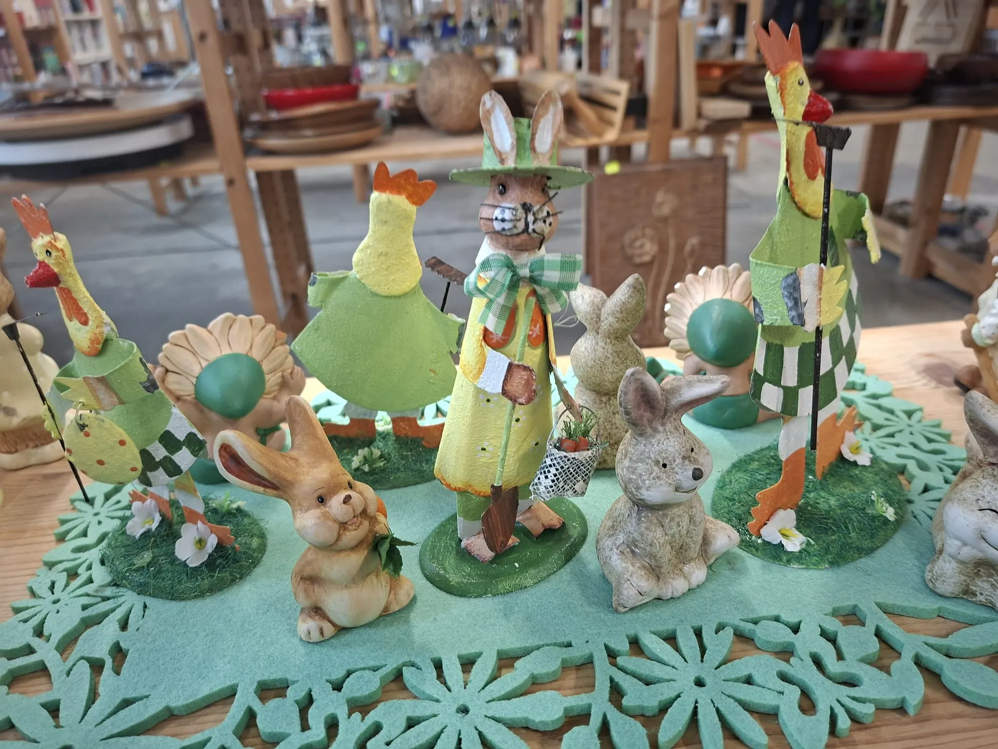 Mehrere bemalte Ostersymbole aus Keramik, darunter Hähne und Hasen, stehen auf einem grün strukturierten Tisch.
