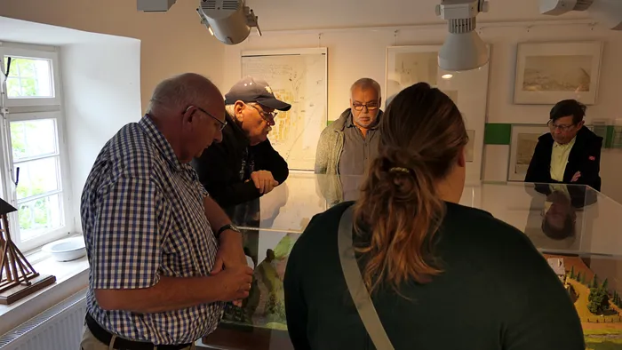 Eine Gruppe von Menschen betrachtet ein Landschaftsmodell in einer Glasvitrine in einem Ausstellungsraum des Heimathauses.