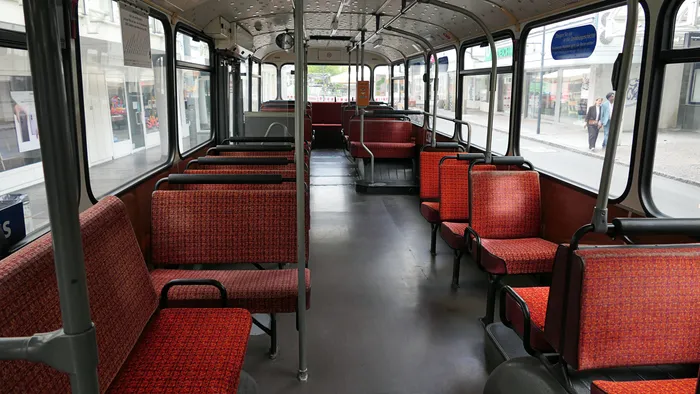 Innenansicht eines historischen Linienbusses mit roten, gemusterten Sitzen und einem Mittelgang.