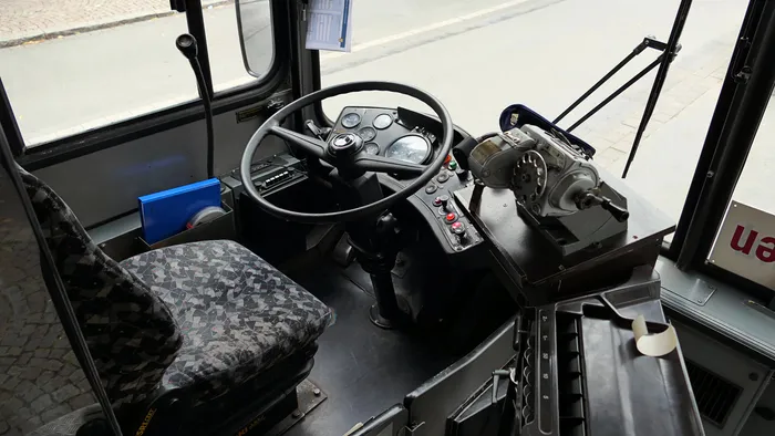 Cockpit eines historischen Linienbusses mit Lenkrad, Armaturenbrett und gemustertem Fahrersitz.