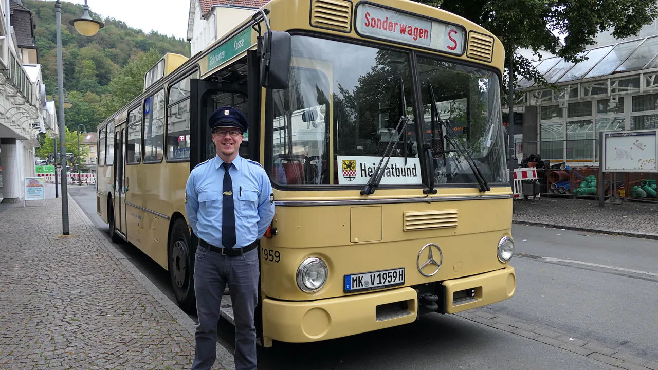 Ein Mann in blauer Uniform steht vor einem historischen gelben Linienbus mit der Aufschrift „Sonderwagen“.