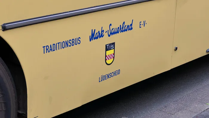 Die Seitenwand eines cremefarbenen Busses mit der Aufschrift „TRADITIONSBUS Mark-Sauerland E.V. LÜDENSCHEID“ und einem Wappen.