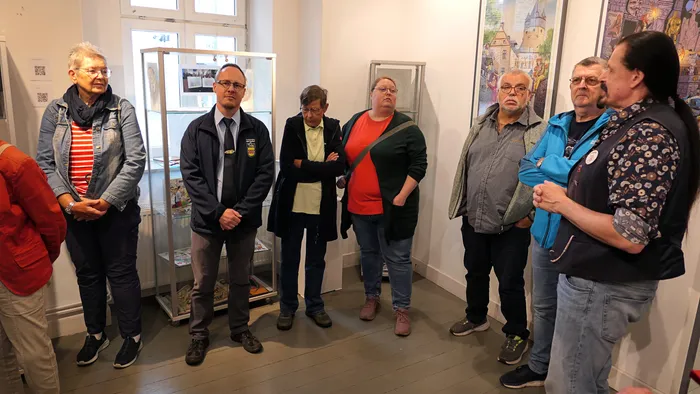 Eine Gruppe von Menschen steht in einem Ausstellungsraum mit einer Glasvitrine und Bildern an der Wand.