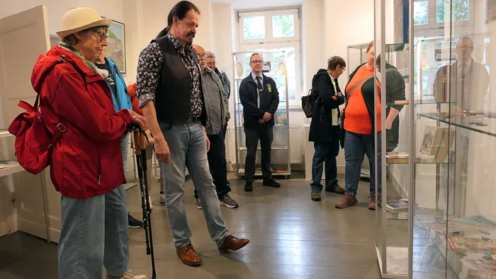 Eine Gruppe von Menschen besichtigt Exponate in Glasvitrinen in einem hellen Ausstellungsraum.