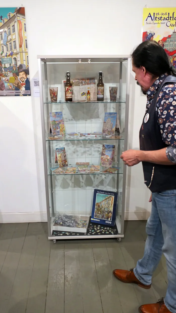Ein Mann betrachtet verschiedene Exponate wie Flaschen und Puzzles in einer Glasvitrine.