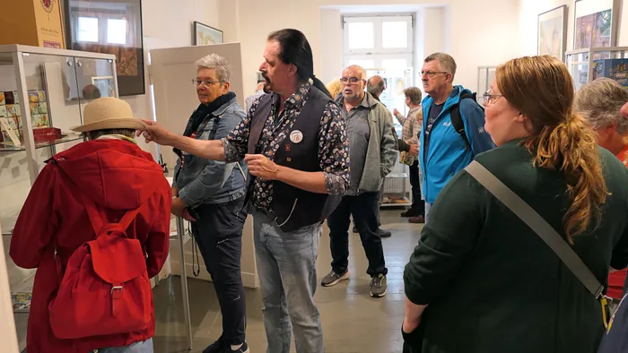 Ein Mann zeigt einer Gruppe von Menschen in einem Ausstellungsraum des Heimathauses auf Exponate in einer Glasvitrine.