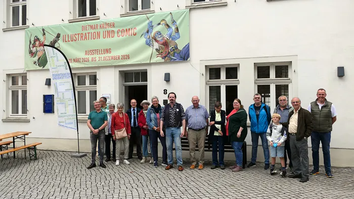 Eine Gruppe von Menschen steht vor dem Heimathaus in Plettenberg vor einem Banner für eine Comic-Ausstellung von Dietmar Krüber.