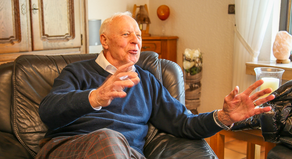 Heinz-Alfred Steiner, ein älterer Mann mit weißen Haaren, sitzt auf einem Ledersofa und gestikuliert beim Sprechen.