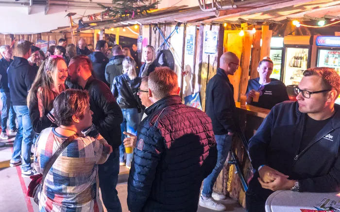 Menschen stehen und unterhalten sich in einer belebten, rustikalen Halle, vermutlich während eines Festes im Feuerwehrgerätehaus Schalksmühle.