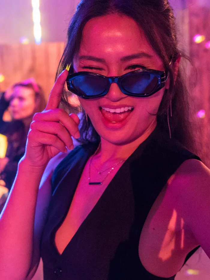 Lachende junge Frau mit dunkler Brille und langen Haaren im Neonlicht einer Party, vermutlich auf der Hüttengaudi im Feuerwehrgerätehaus Schalksmühle.