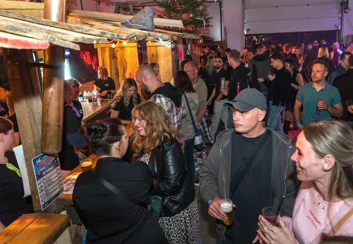 Menschen stehen und unterhalten sich an einer Bar in einem voll besetzten Raum, vermutlich auf einem Fest im Feuerwehrgerätehaus.