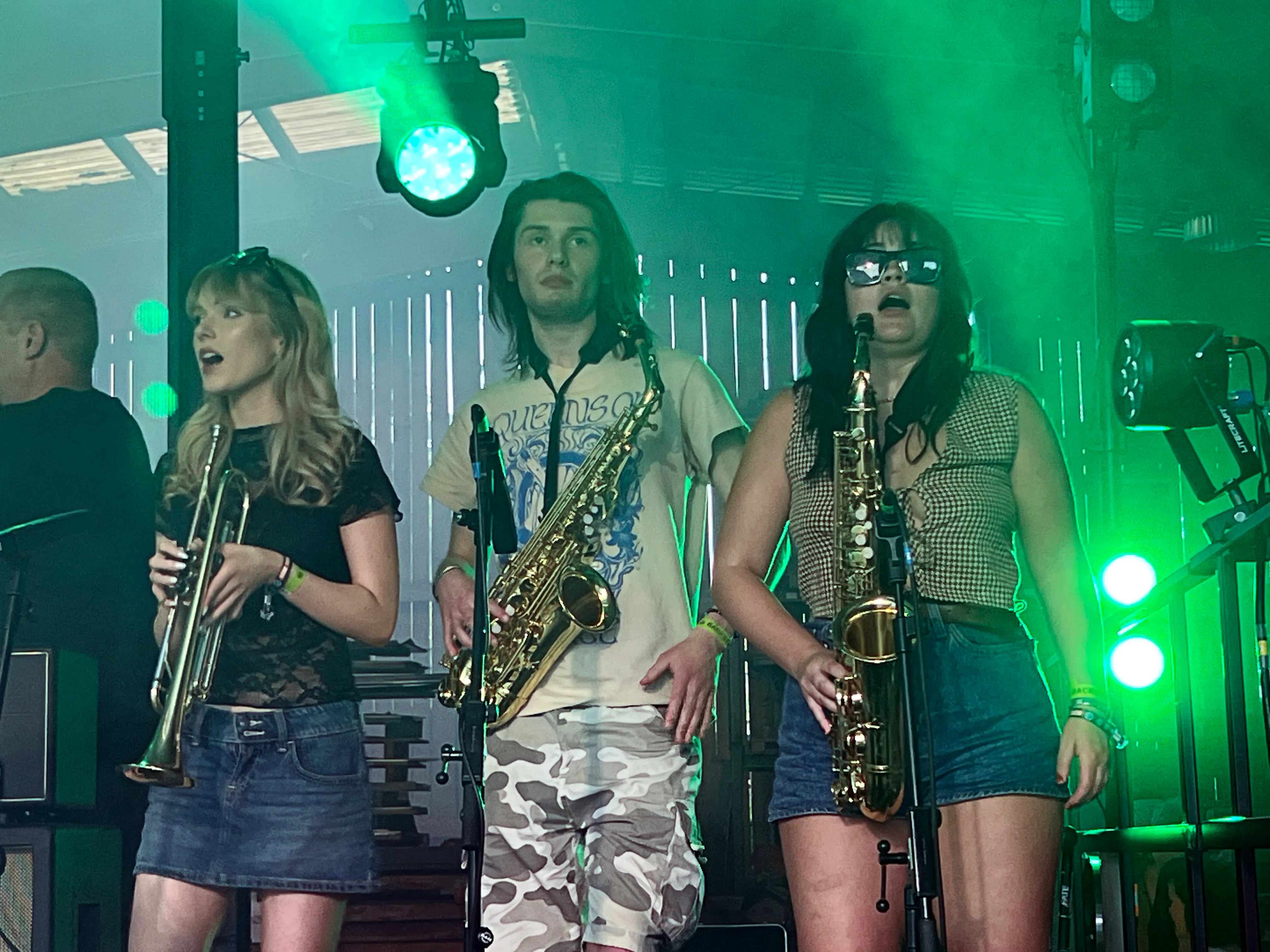 Drei Musiker spielen auf einer Bühne Saxophone. Im Hintergrund grüne Bühnenbeleuchtung und Scheinwerfer.