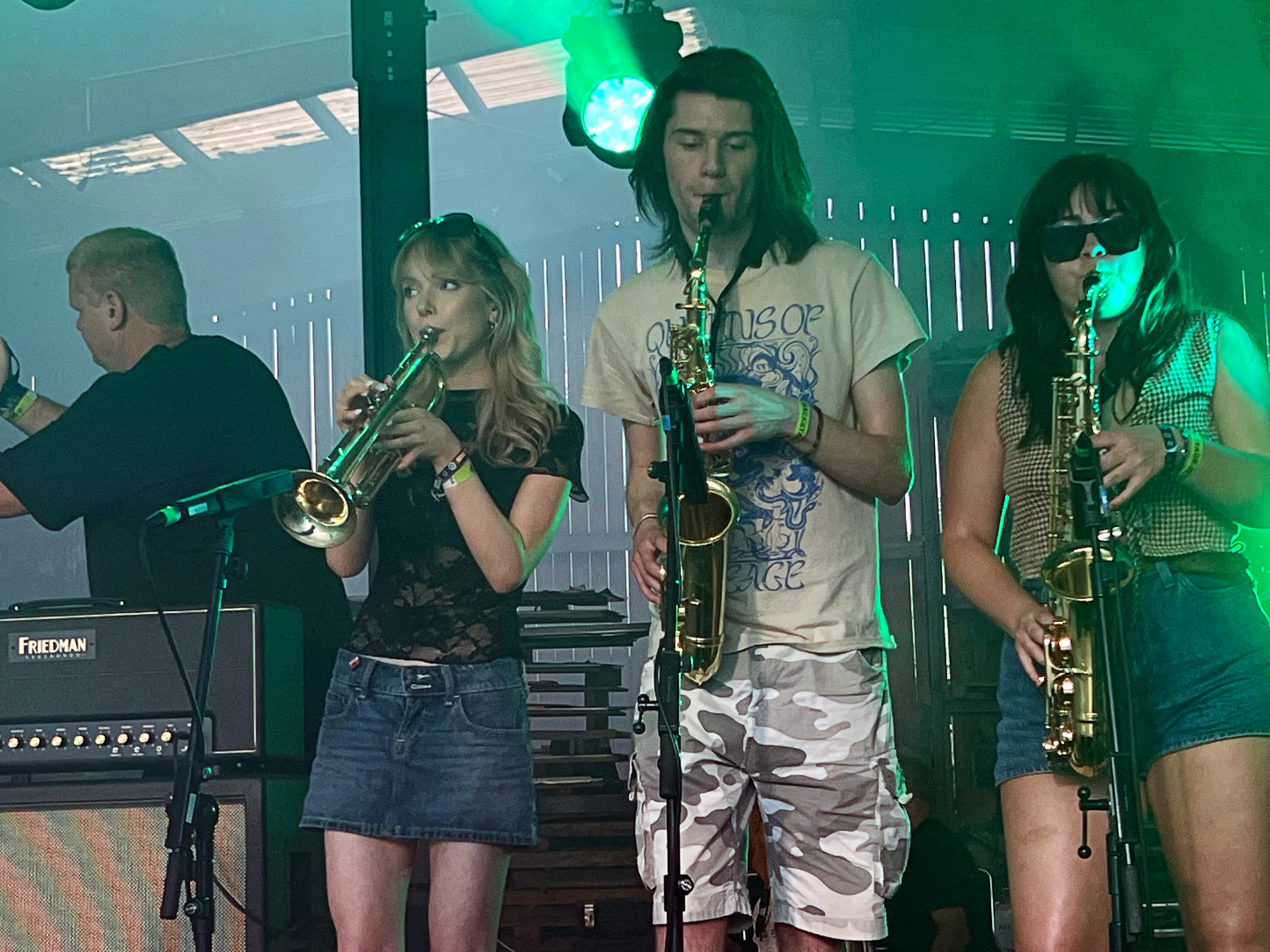 Vier Musiker spielen auf einer Bühne Saxophone und Posaune. Im Hintergrund grüne Bühnenbeleuchtung und Verstärker.