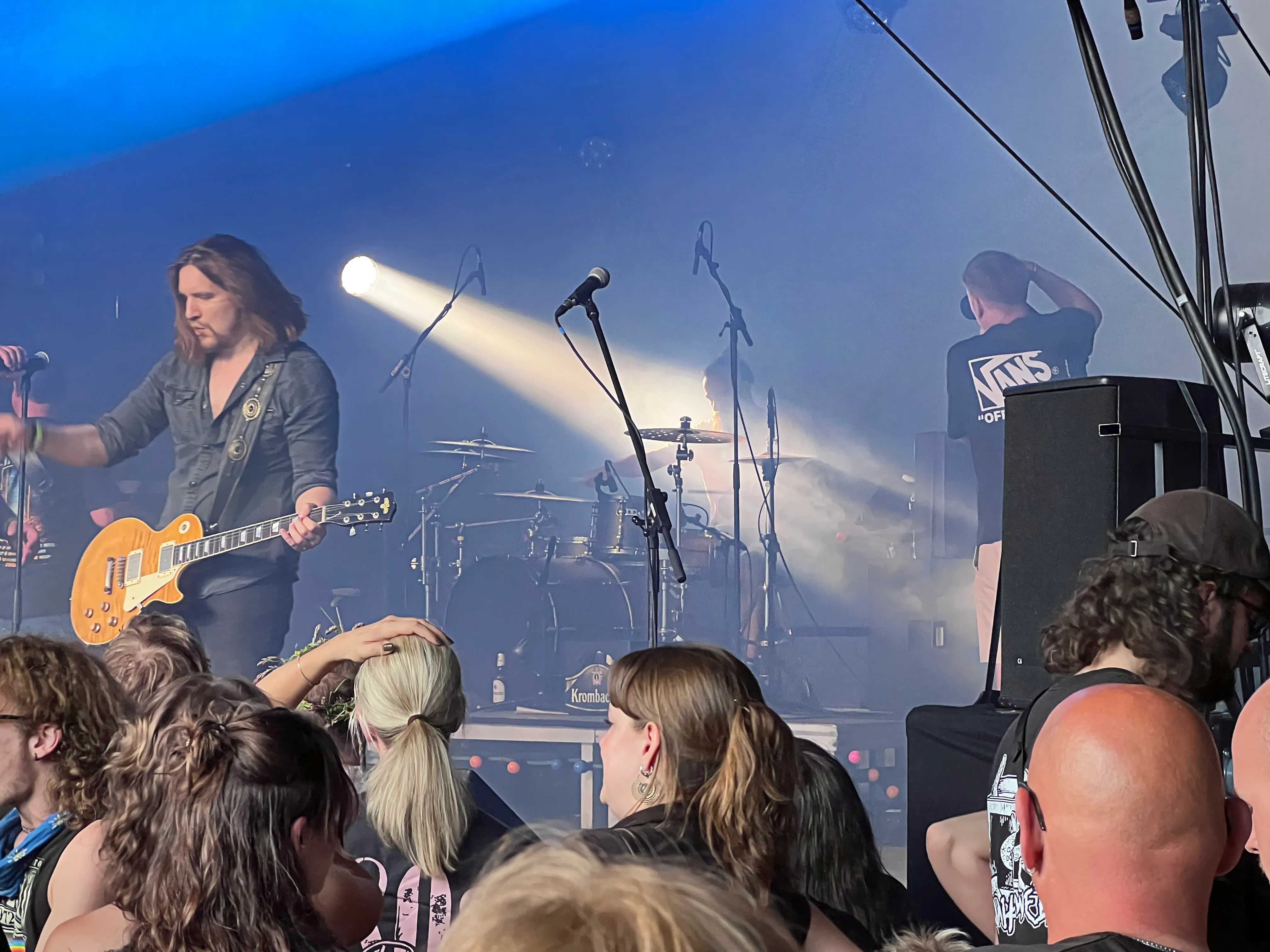 Bühnenbild des I-Rock Festivals mit einem Gitarristen im Vordergrund und einem Schlagzeuger im Hintergrund, vor einem Publikum.