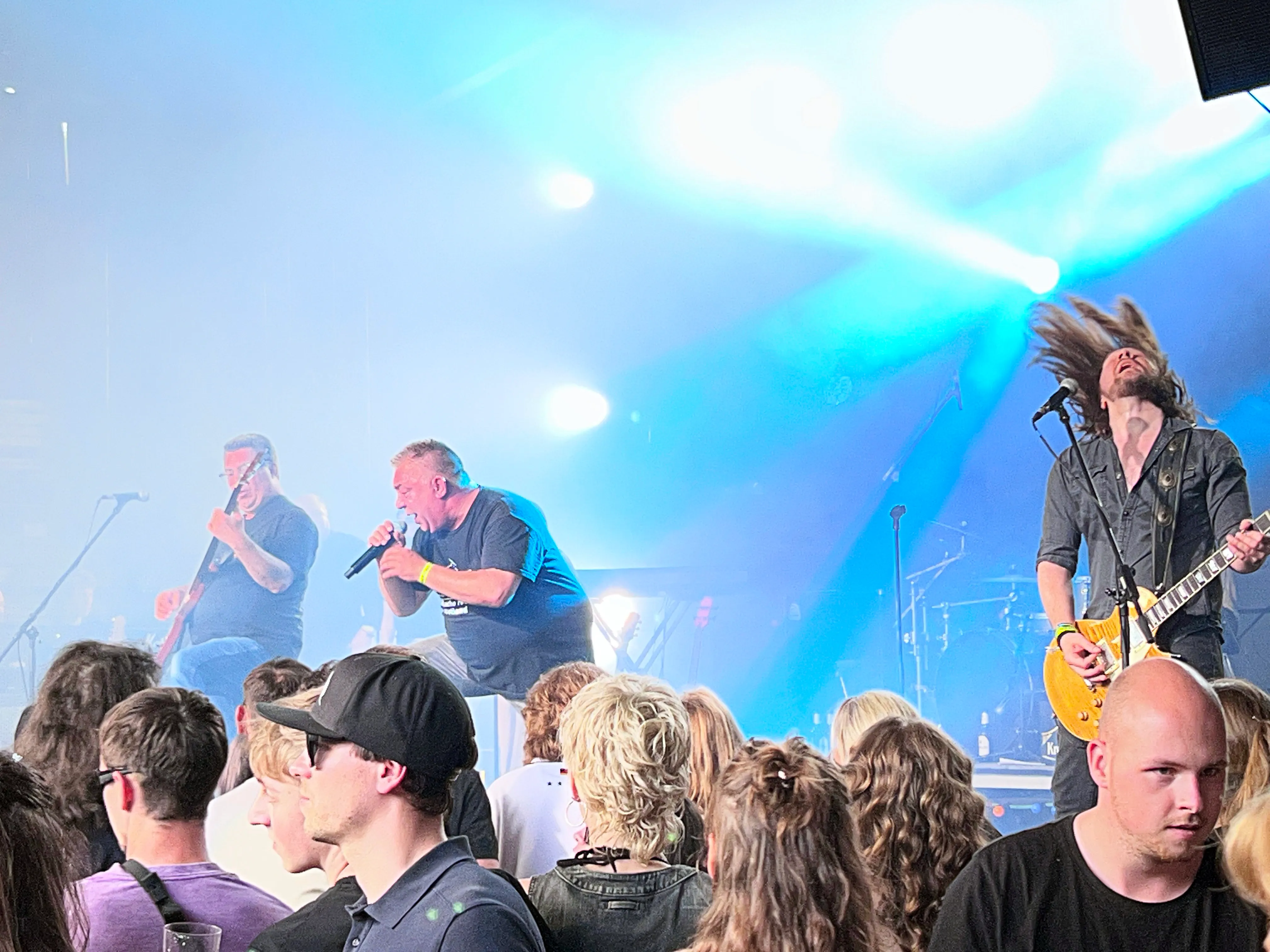 Rockband spielt vor begeistertem Publikum auf dem I-Rock Festival in Plettenberg. Ein Gitarrist mit wehenden Haaren ist im Vordergrund zu sehen.