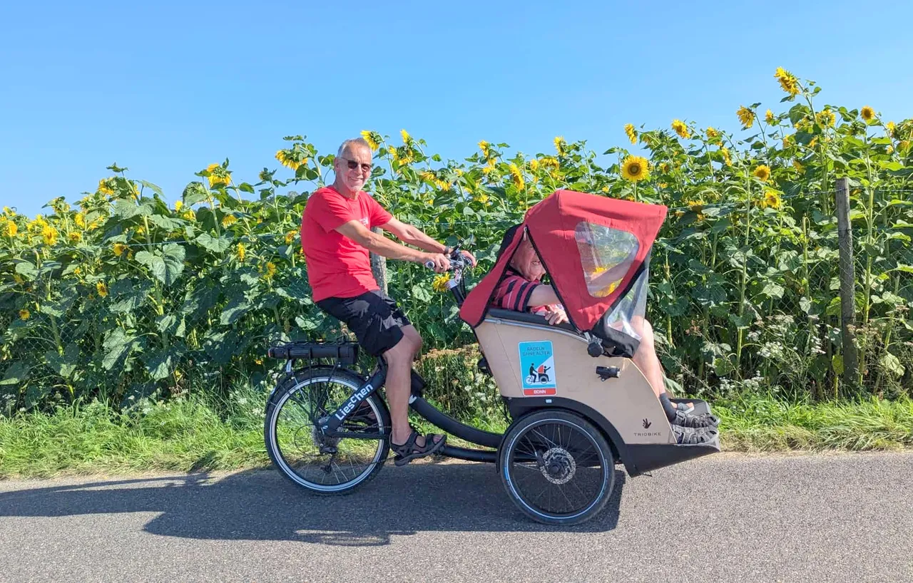 Ein Mann fährt ein Kind in einer Fahrradrikscha durch ein Feld voller Sonnenblumen.