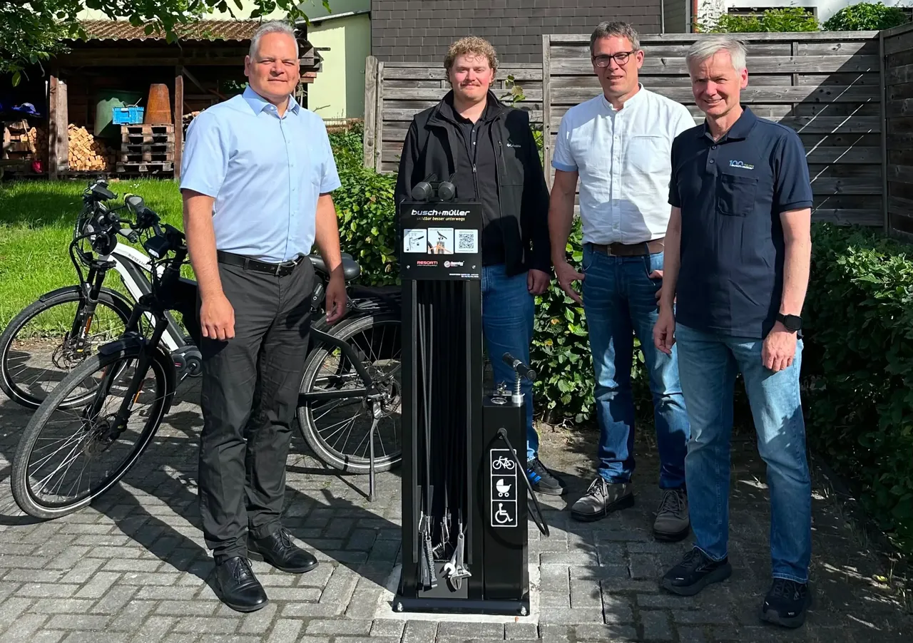 Vier Männer stehen vor einer Luftpumpe für Fahrräder und einem Gebäude mit einem Kirchturm im Hintergrund. Von links nach rechts sind es Bürgermeister Olaf Stelse, Guido Müller, Klimaschutzmanager Bastian Vollmann und Fachbereichsleiter Lars Feltens von der Stadt Kierspe.
