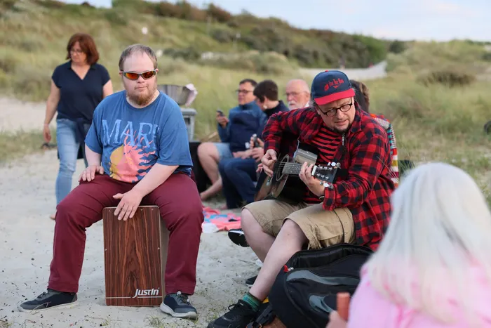 Zwei Männer spielen Musik am Strand, einer auf einem Cajon und einer auf einer akustischen Gitarre.