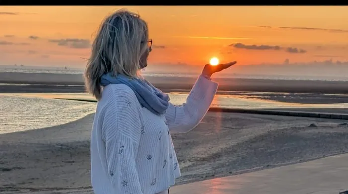 Eine Frau hält bei Sonnenuntergang am Meer die Sonne in ihrer ausgestreckten Hand.