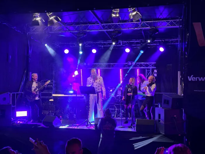 Eine Band tritt unter blauem und violettem Bühnenlicht bei einem Gemeindefest auf.