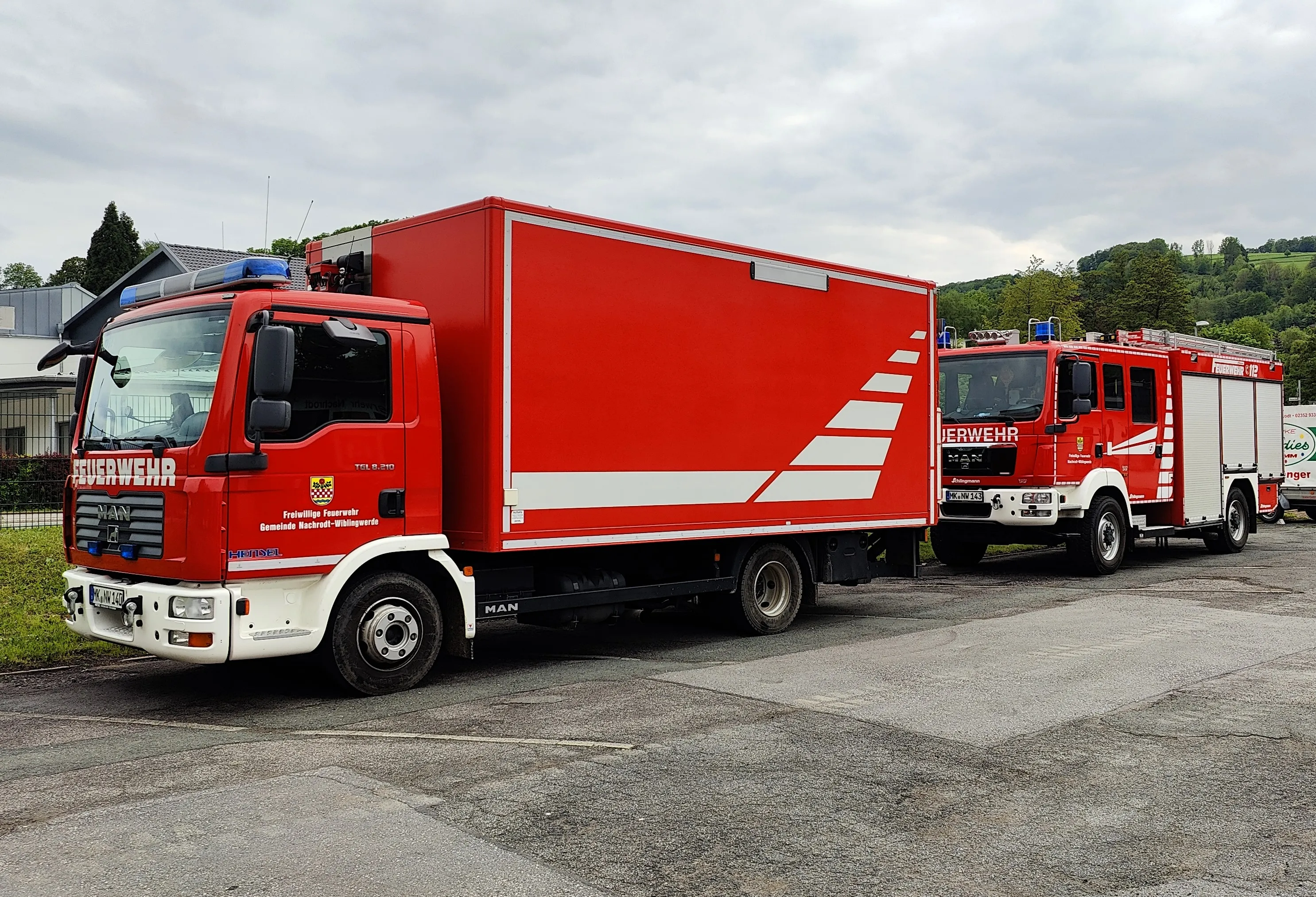 Zwei rote Feuerwehrautos der Freiwilligen Feuerwehr Nachrodt-Wiblingwerde stehen auf einem Parkplatz.