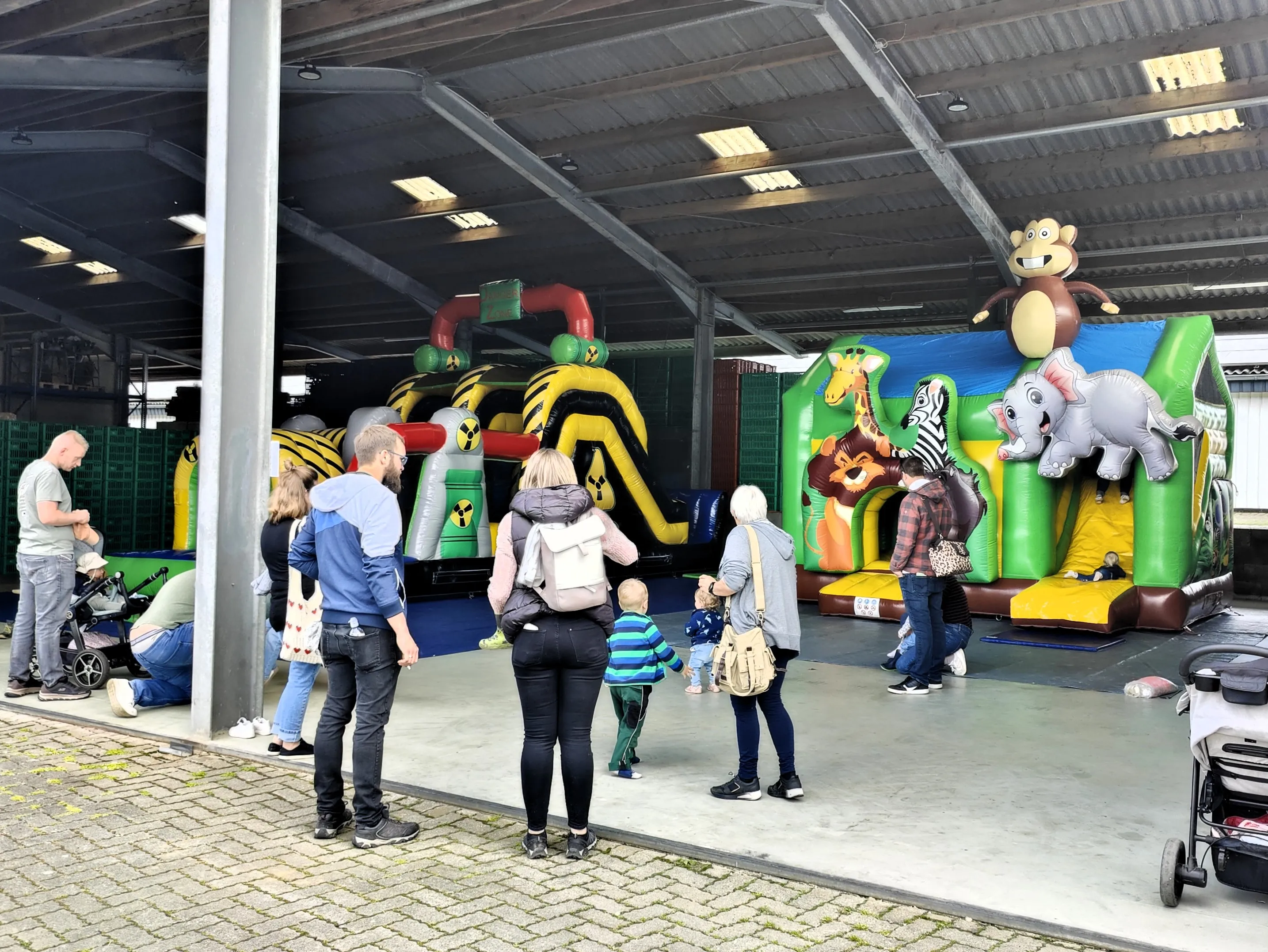 Menschen stehen und schauen auf mehrere aufblasbare Hüpfburgen mit Tiermotiven in einer großen Halle auf dem Geflügelhof Gieseker.