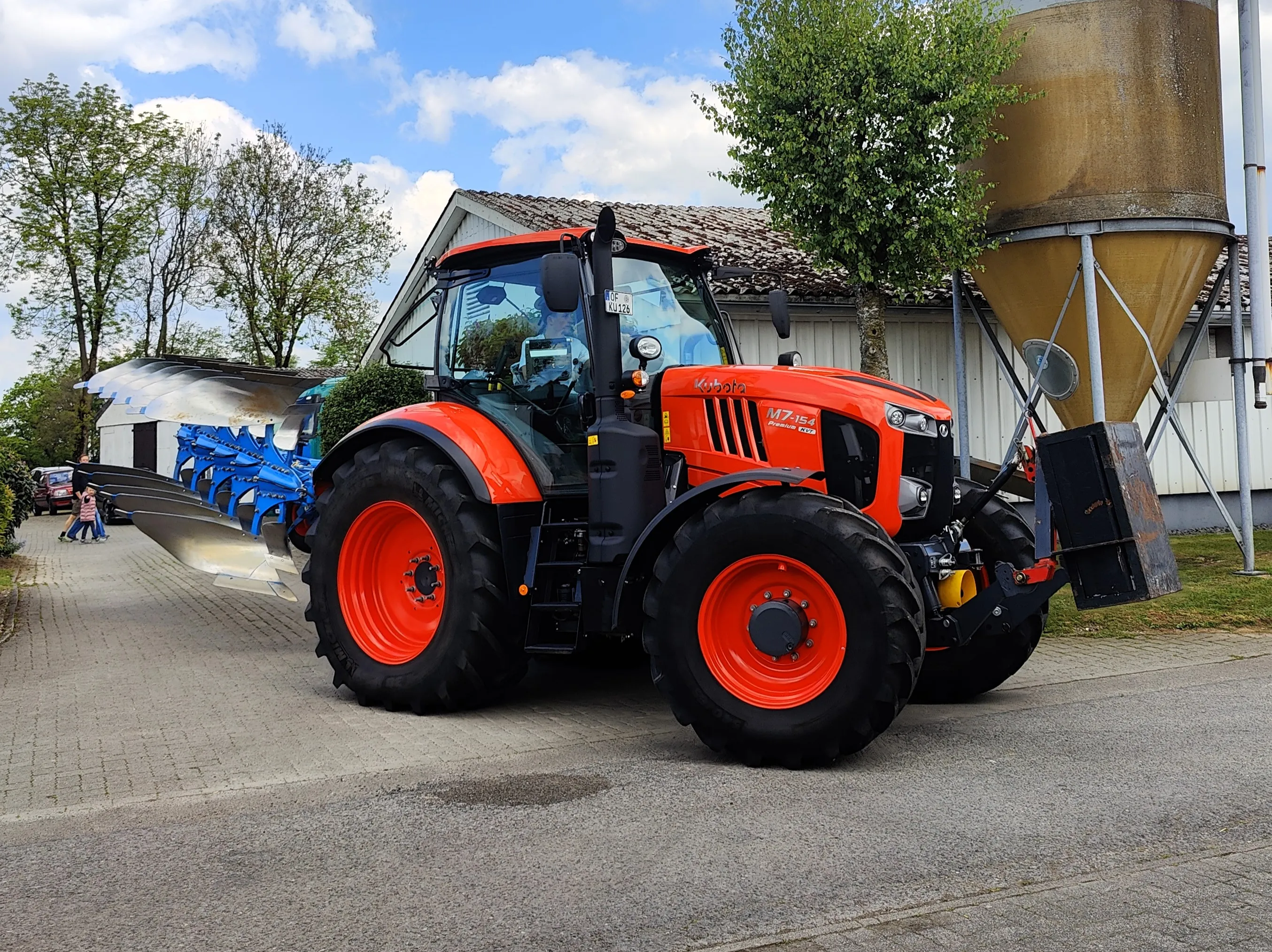 Oranger Traktor mit blauem Pflug steht auf dem Hof Gieseker vor großen Silos.