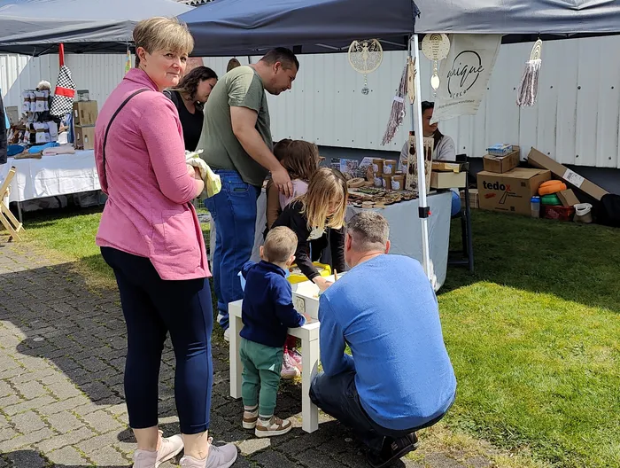 Mehrere Personen betrachten und kaufen Waren an einem Stand auf einem Markt oder einem Bauernhof, darunter auch Kinder.