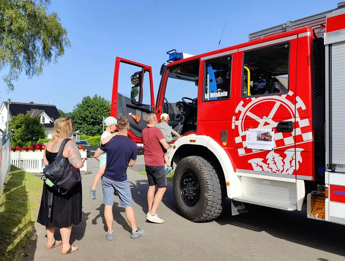 Roter Feuerwehrauto mit der Aufschrift „Winkeln“ steht auf einer Wiese, umgeben von Besuchern eines Dorffestes.