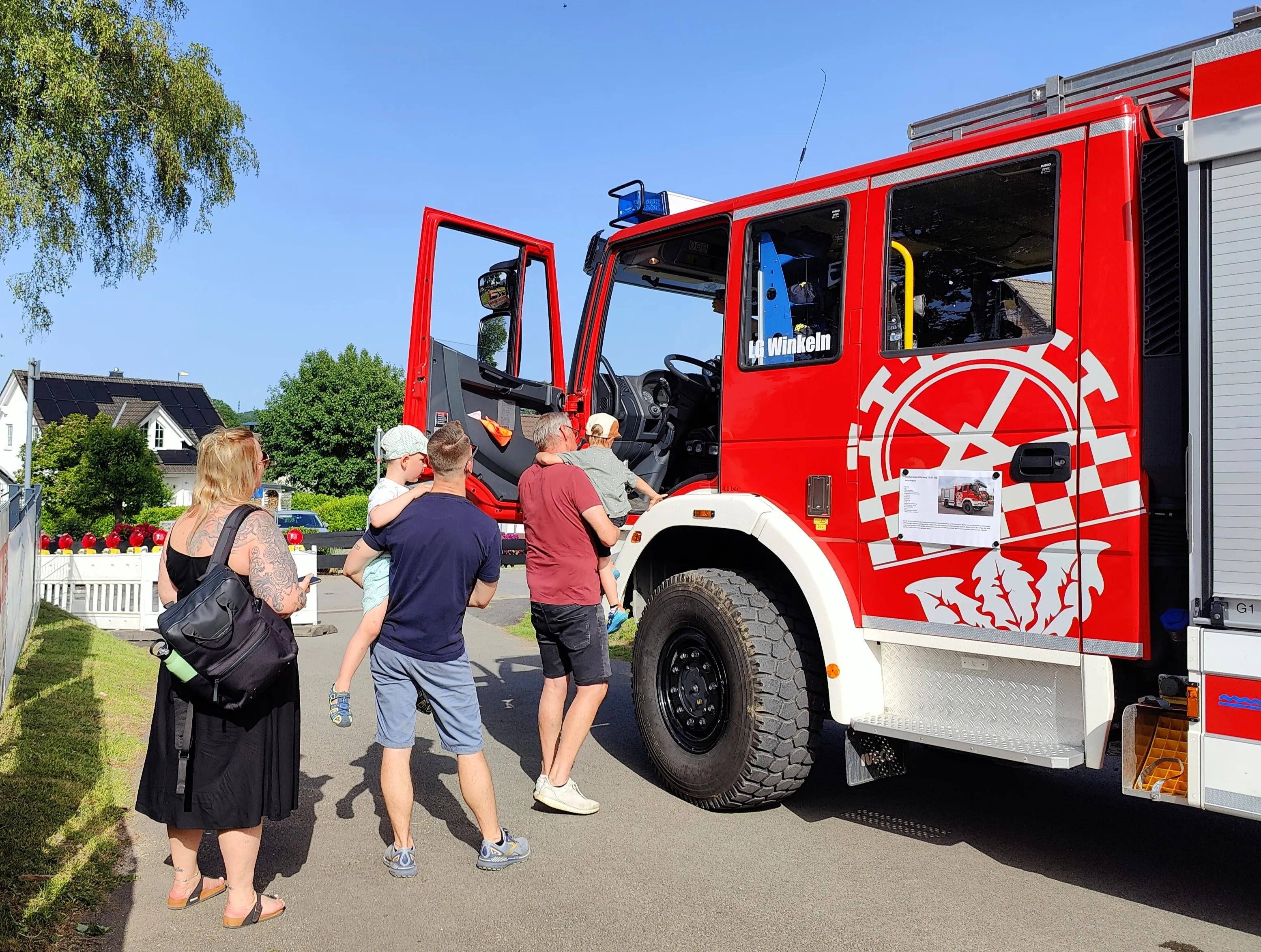 Roter Feuerwehrauto mit der Aufschrift „Winkeln“ steht auf einer Wiese, umgeben von Besuchern eines Dorffestes.