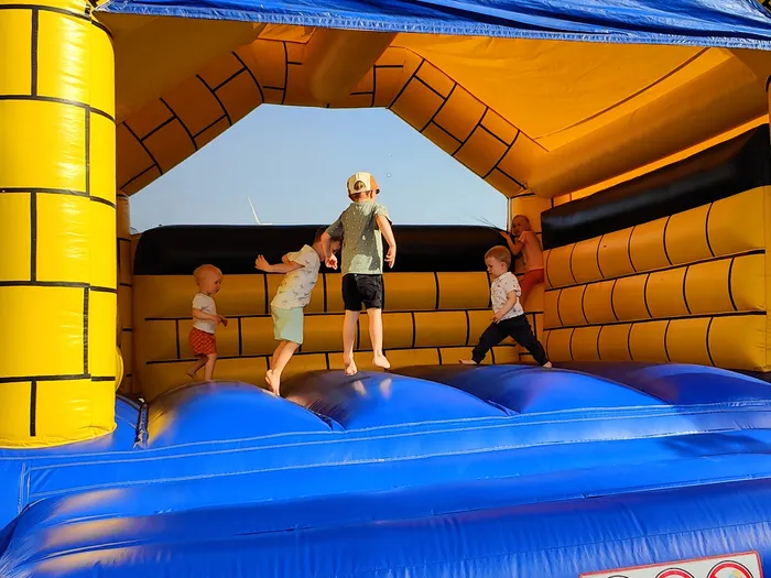 Drei Kinder spielen und springen auf einer blauen Hüpfburg mit gelben und schwarzen Burgmauern.
